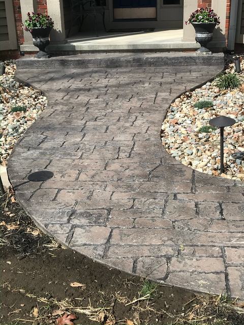 Curved cobblestone-style stamped concrete walkway leading to a brick home with planters