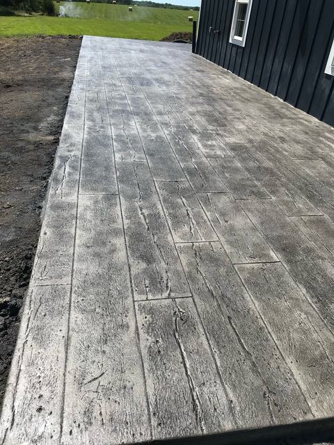Wood-plank stamped concrete patio alongside a dark navy home with countryside views